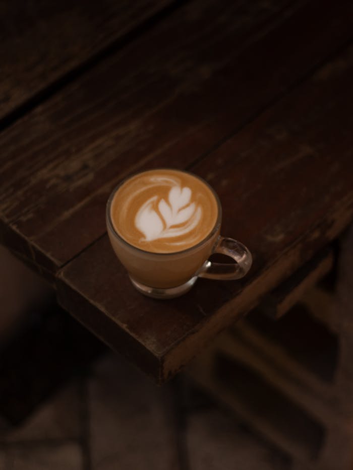 A cup of coffee with intricate latte art on a vintage wooden table, perfect for cozy cafe vibes.